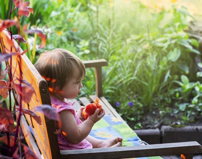 Child eating peach on garden bench